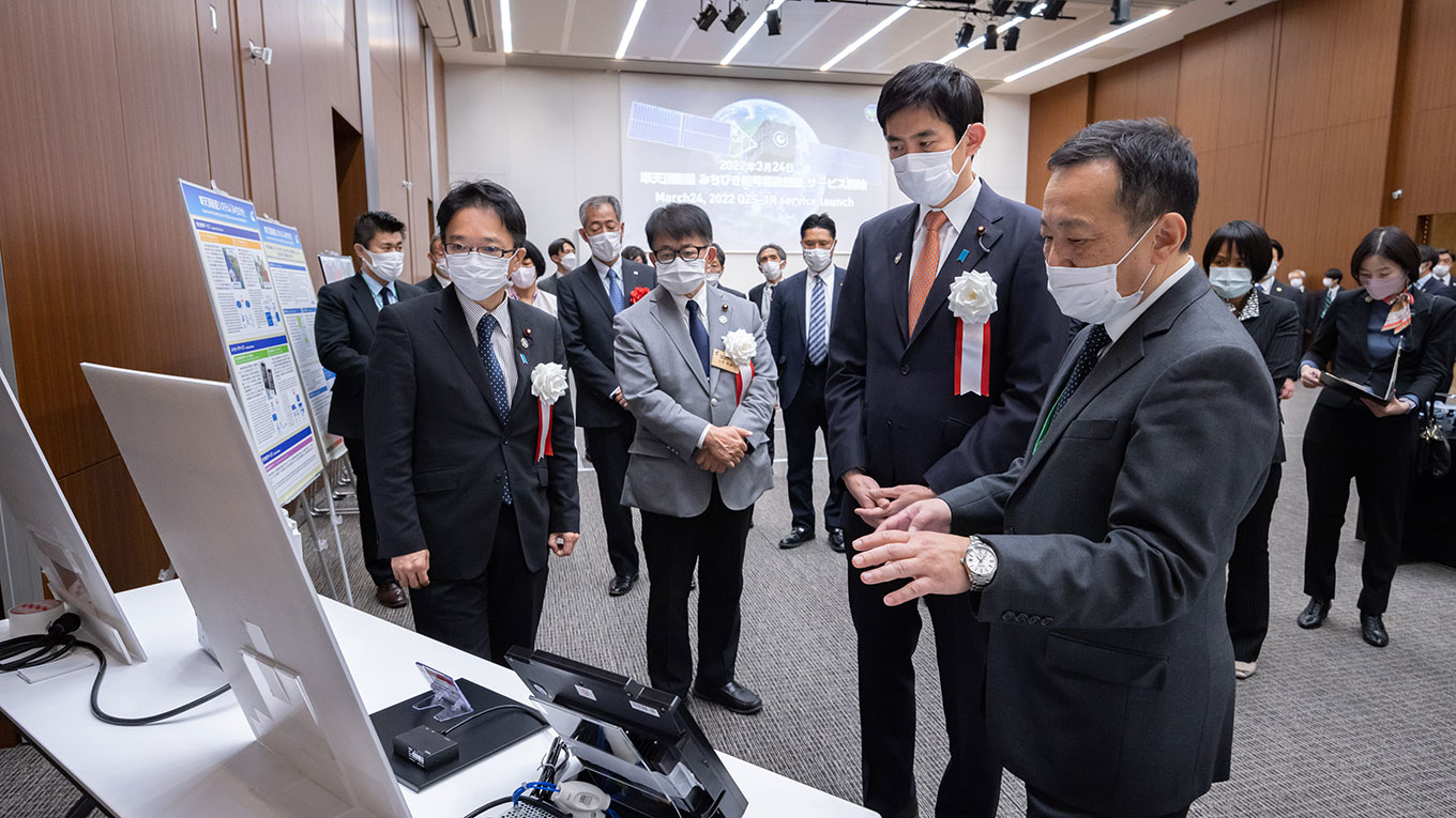 [写真：展示会場を視察する小林大臣ら]