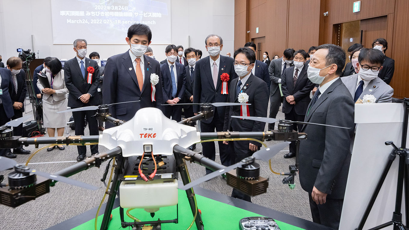 [写真：みちびき対応ドローンについて説明を受ける小林大臣]